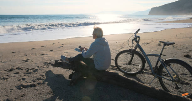 istock Mature man pauses by water's edge with bicycle, uses mobile phone 2186965241