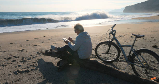 istock Mature man pauses by water's edge with bicycle, uses mobile phone 2186965250