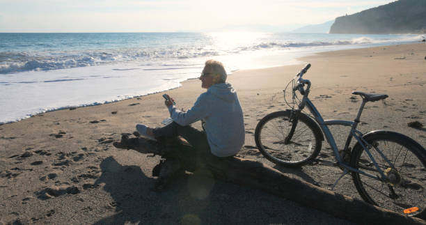 istock Mature man pauses by water's edge with bicycle, uses mobile phone 2186965274