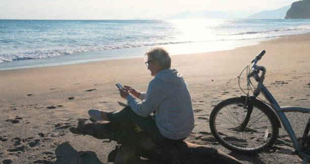 istock Mature man pauses by water's edge with bicycle, uses mobile phone 2186965275