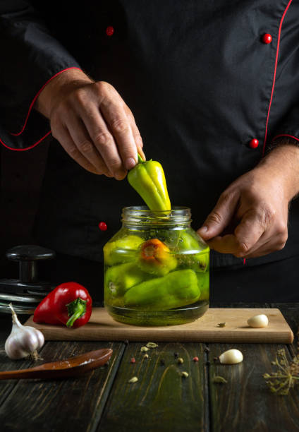 istock Talented chef skillfully adds vibrant green peppers into a glass jar, preparing a flavorful pickling process. The warm, rustic kitchen atmosphere enhances the culinary experience 2186965308