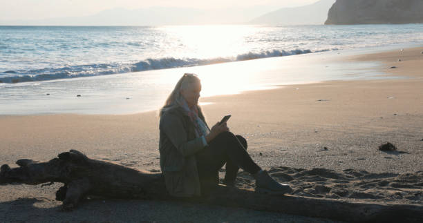 istock Mature woman uses phone on beach at sunset 2186965399