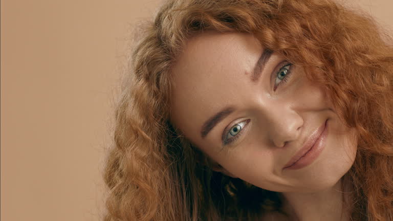 Young woman with curly red hair poses against a neutral background