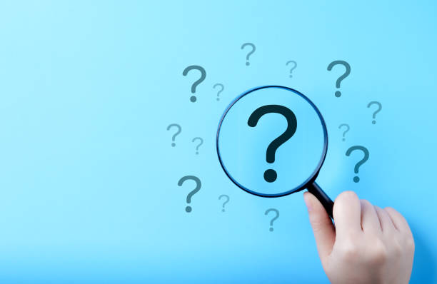 istock Question Mark and Root Cause Analysis Concept. A hand holding a magnifying glass over a large question mark surrounded by smaller ones on a blue background, symbolizing analysis and problem-solving. 2186968899