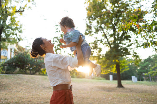 istock Mother lifting young child in sunny, green park setting 2186975411