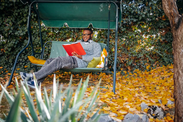 Smart child girl, 8-9 years old, in jacket hat glasses, reading book, on play area on spring day.