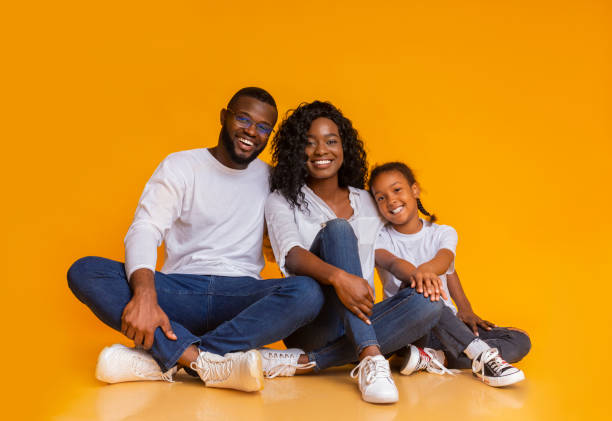 istock Smiling african family sitting on floor over yellow studio background 2186978109