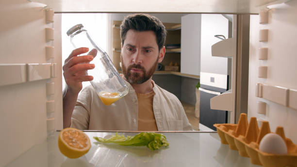 istock Man open empty refrigerator with half lemon lettuce leaf one egg slice of bread leftover orange juice in bottle find solution order food delivery with mobile phone app point of view from inside fridge 2186987548