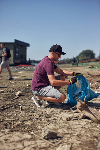 istock Environmental activist cleaning river shore from piled up trash. 2186998016