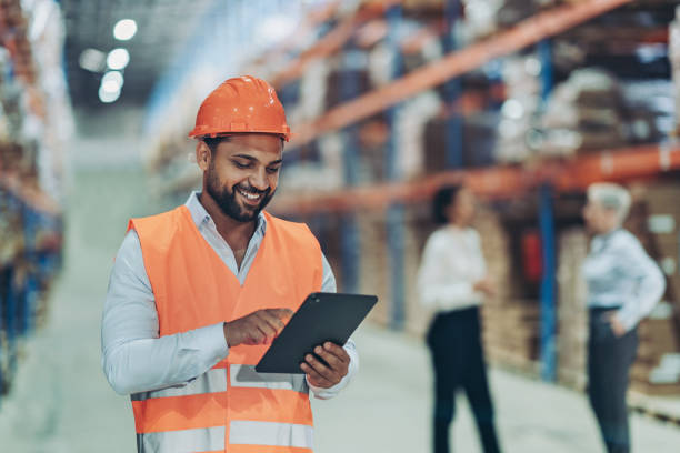 istock Businessman with digital tablet, protective helmet and reflective vest working in a warehouse 2186999008