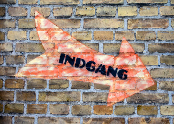 A Danish sign reading ‘Indgang’, meaning ‘Entrance’, with a colourful arrow on a brick wall.