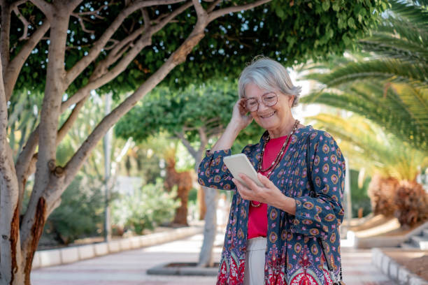 istock Smiling senior woman in public park while using mobile phone, caucasian elderly lady enjoying free time in retirement 2187002259