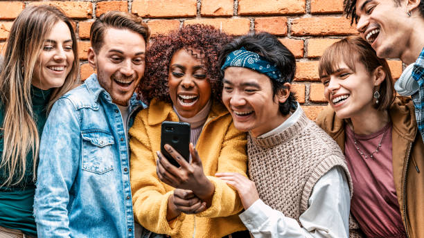 istock Happy group of multiracial teens using smart mobile phone outdoors front of the wall - Diverse university students watching smartphones in college campus - Millenial people having fun on city street 2187005881