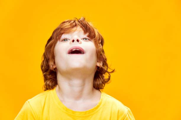 Red-haired boy looking up with open mouth surprise yellow background