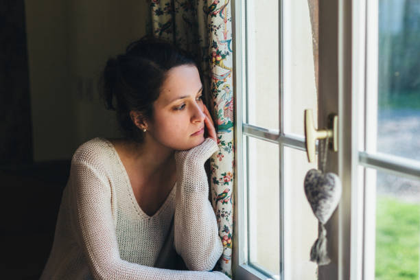 istock Depressed woman looking through window 2187011811