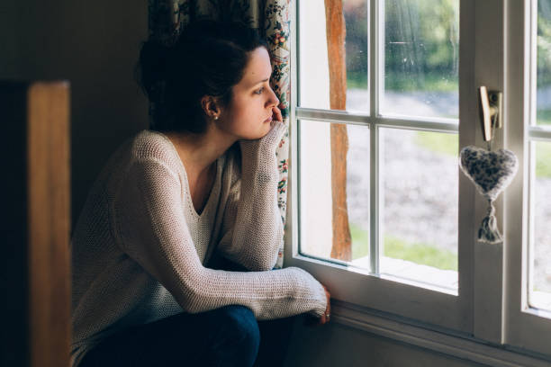 istock Depressed woman looking through window 2187011878