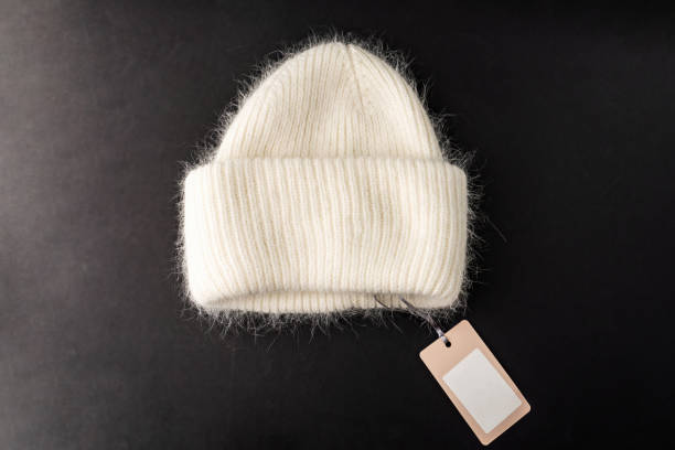 istock cozy, fluffy white wool hat hangs elegantly against a dark backdrop, highlighting comfort and warmth. The tag on a string invites curiosity about its origin and craftsmanship 2187018629