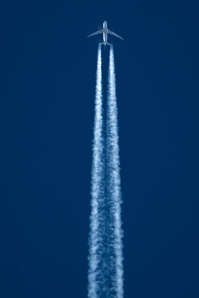 Passenger jet flies overhead with jet stream portrait view with deep blue sky background.