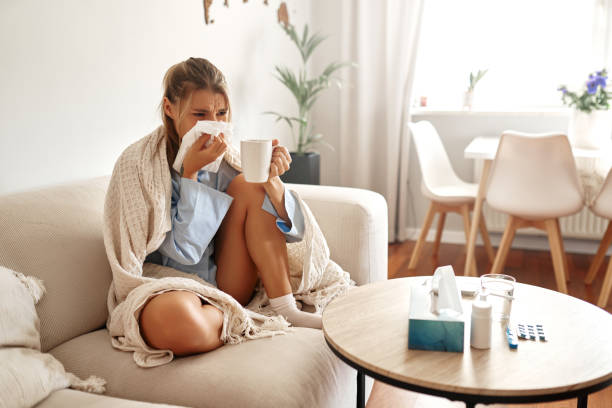 istock A young woman feeling unwell is wrapped snugly in a blanket while sitting on her couch 2187026341