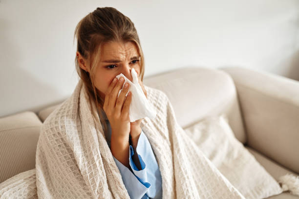 istock A young woman feeling unwell is wrapped snugly in a blanket while sitting on her couch 2187026346