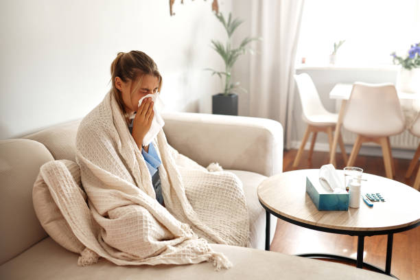 istock A young woman feeling unwell is wrapped snugly in a blanket while sitting on her couch 2187026363
