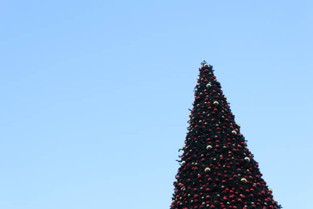 A stunning Christmas tree adorned with ornaments under a bright blue sky, perfect for holiday celebrations.
