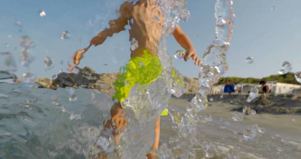 A joyful child runs through shallow water at the beach, making playful splashes in the background