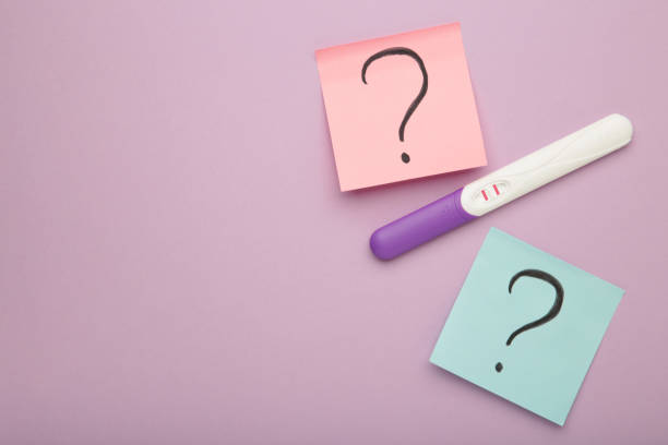 istock Pregnancy test with two stripes with question marks on purple background. 2187027170