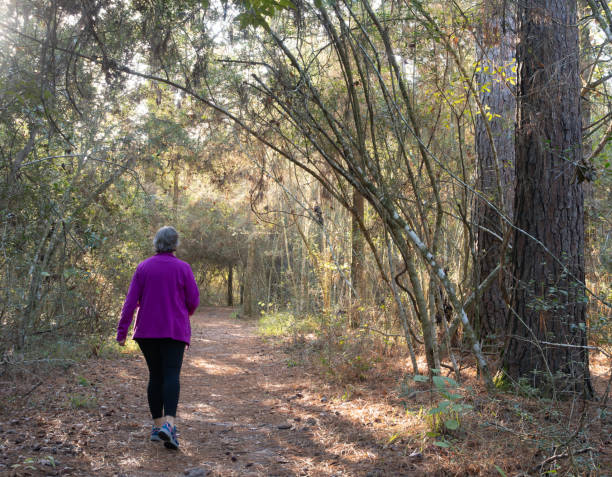 istock Senior Woman Walking Along Wooded Pathway with Back to Camera 2187029589