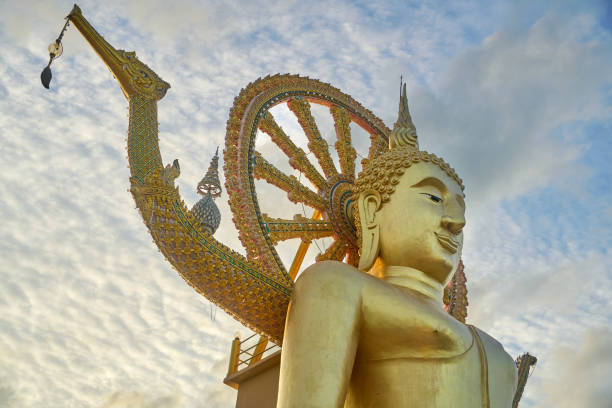 A stunning golden Buddha statue adorned with intricate details and surrounded by a serene sky. Located in Koh Samui, Thailand, this iconic landmark is a popular destination for tourists and pilgrims alike, offering a peaceful atmosphere.