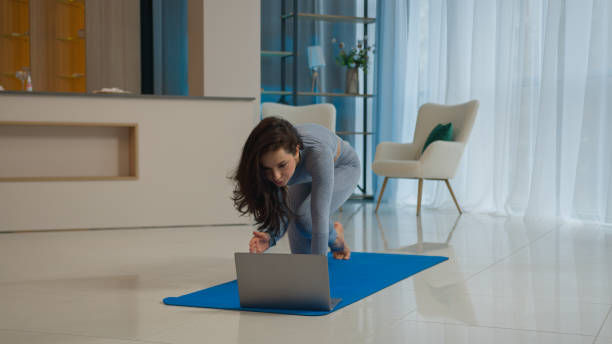 istock Yoga class with laptop workout video tutorial online training at home fit Caucasian woman sport trainer girl yogi female sportswoman doing exercise raise leg hand learning asana fitness pilates on mat 2187040607