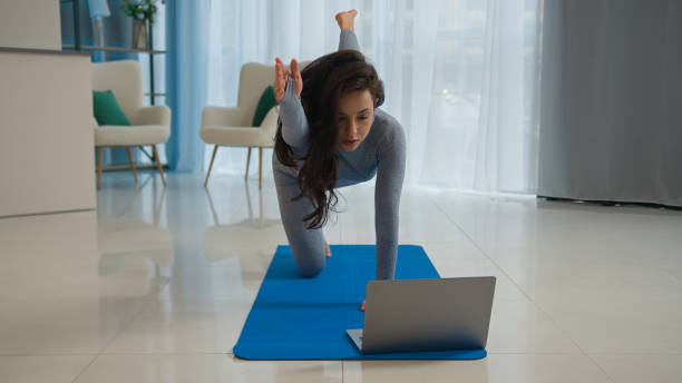 istock Yoga class with laptop workout video tutorial online training at home fit Caucasian woman sport trainer girl yogi female sportswoman doing exercise raise leg hand learning asana fitness pilates on mat 2187041965