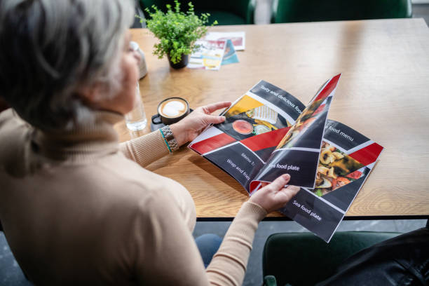 istock Elderly woman browsing colorful menu at cozy cafe. 2187043363
