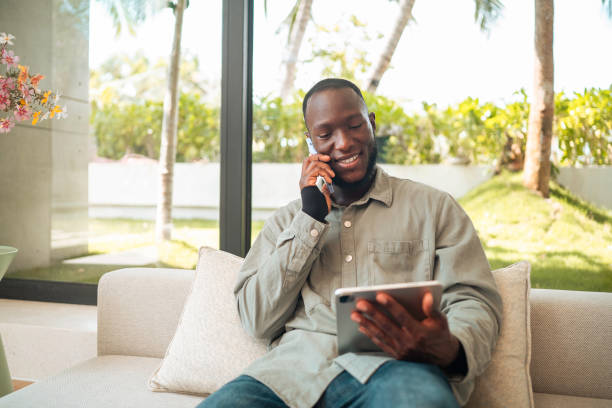 istock Cheerful Black Man Multitasking with Phone and Tablet at Home 2187047334