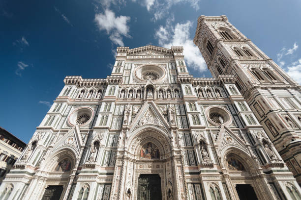A breathtaking upward view of the Florence Cathedral’s intricate marble facade and its adjacent bell tower, the Campanile di Giotto. The vibrant details of the Gothic architecture stand out against the bright blue sky, highlighting the grandeur of this iconic Renaissance landmark in Italy.