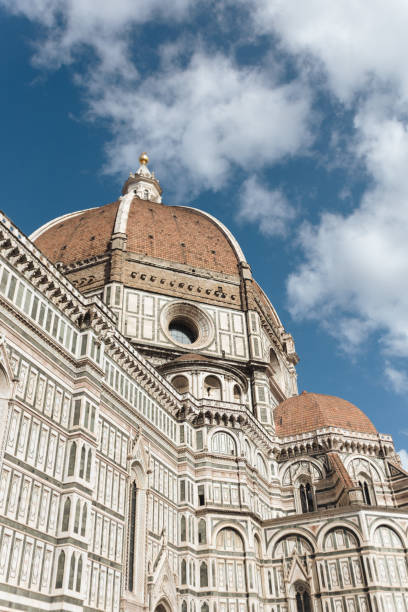 A striking perspective of the iconic dome of the Florence Cathedral, also known as the Duomo, in Florence, Italy. The intricate marble facade and terracotta roof stand out under a bright sky, showcasing the grandeur of Renaissance architecture and its historical significance.