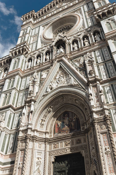 A breathtaking upward view of the Florence Cathedral’s intricate marble facade and its adjacent bell tower, the Campanile di Giotto. The vibrant details of the Gothic architecture stand out against the bright blue sky, highlighting the grandeur of this iconic Renaissance landmark in Italy.