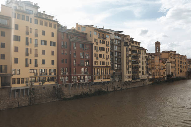A scenic view of the buildings along the Arno River in Florence. The contrasting colors of the architecture stand out against the backdrop of the river, with a soft, natural light enhancing the peaceful atmosphere. The mix of modern and traditional buildings reflects the unique blend of history and contemporary life in Florence.