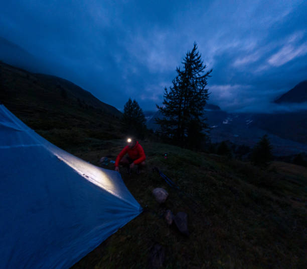 istock Camper adjusting tent with headlamp in dark mountain landscape 2187071333