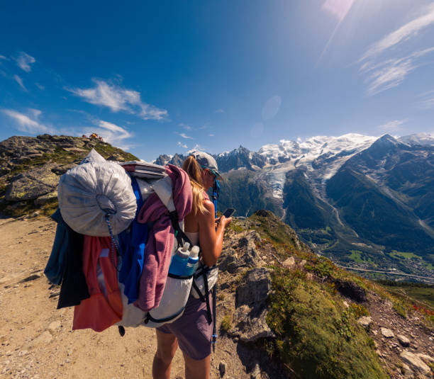 Woman with large backpack on rocky trail looking at stunning mountain range, engaged in adventure. Scenic trekking, nature exploration, and outdoor travel.