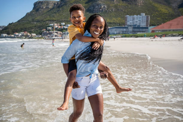 Happy, black family and child with mom on beach for vacation, holiday or weekend in nature. Kid, son and smile with mother on ocean coast, sandy shore or sea for travel, trip or childhood together