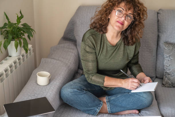 istock Smiling Mature Female, Taking Notes And Planning, Relaxing On Couch By Window With Natural Light, Writing Goals And Organizing Schedule, Productivity Concept Indoors 2187078813