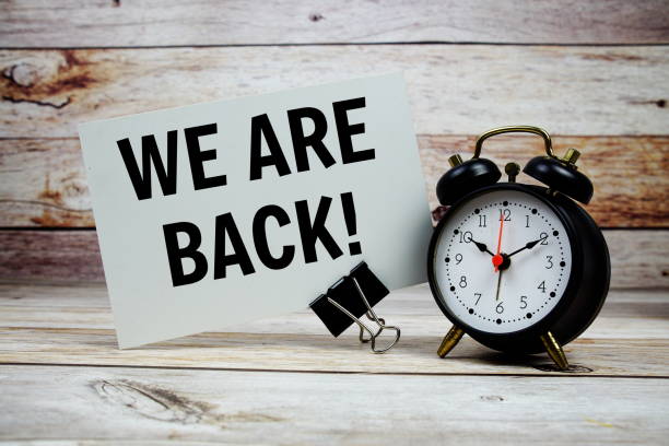 istock We are Back text on paper card with alarm clock on wooden background 2187082372