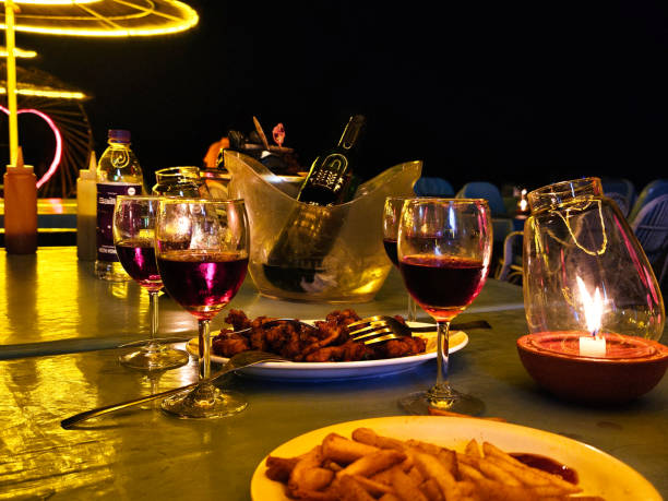 Calangute Goa A dinner setup on a table featuring wine glasses, a bottle of wine in an ice bucket, candlelight, and a plate of food with fries, creating a cozy dining experience.