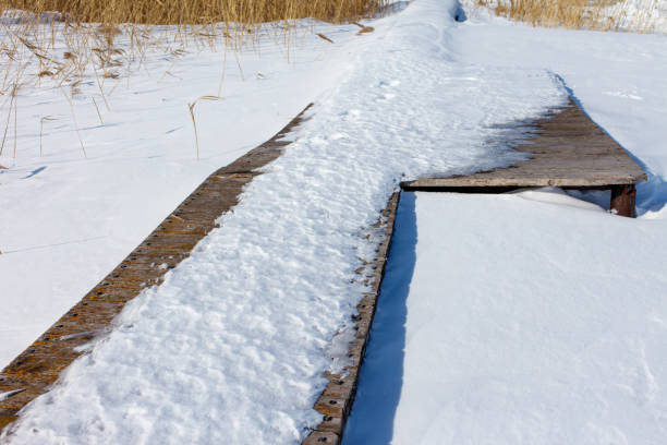 A wooden bridge covered in snow. The snow is piled up on the bridge and the ground. The bridge is in the middle of a field