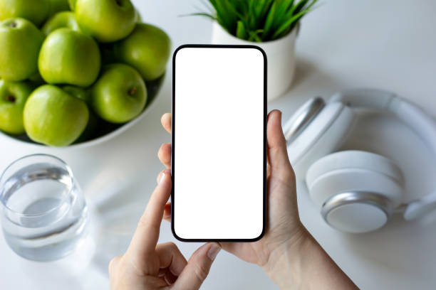 istock hands holding phone isolated screen white table with  green apples 2187084353