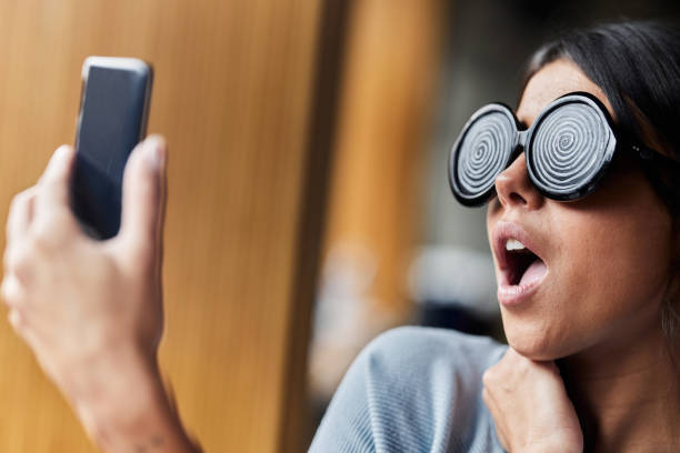 Shocked woman with hypnotic eyeglasses being controlled while taking a selfie with cell phone.