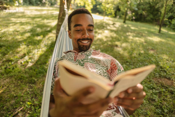 istock Young man relaxing in hammock reading a book in garden 2187087111