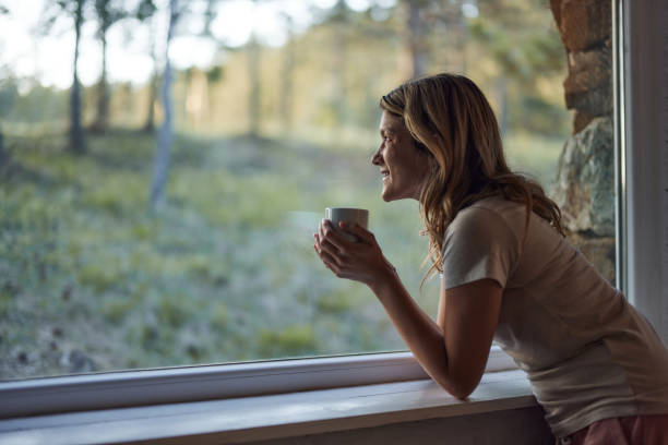 istock Pensive woman looking through window during coffee time at home. 2187087684