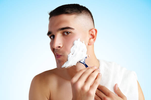 Young handsome man applying shaving foam against white background